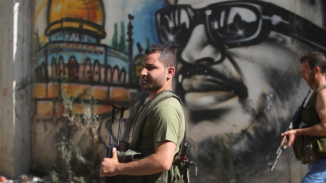 Palestinian gunmen from the Fatah movement, hold their weapons as they walk in front of graffiti of late Palestinian leader Yasser Arafat, at Ein el-Hilweh Palestinan refugee camp, in the southern port city of Sidon, Lebanon, Staurday, July 25, 2015. AP