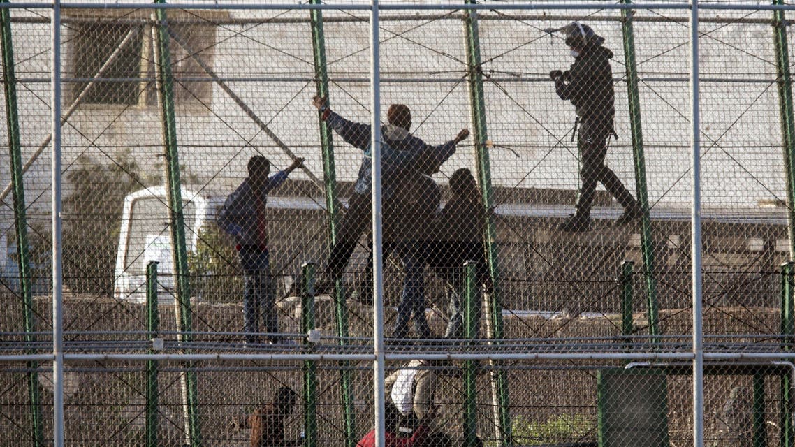 Sub-Saharan migrants argue with Spanish police officers as they sit on a metallic fence that divides Morocco and the Spanish enclave of Melilla, Spain, Friday, Oct. 31, 2014. AP