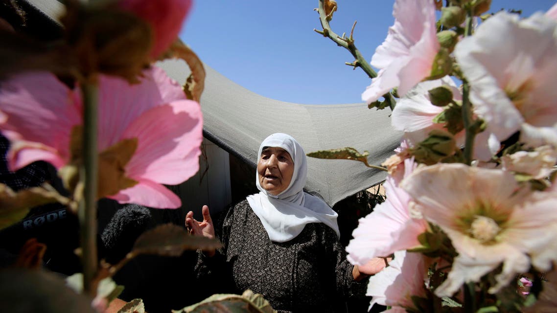 In this Wednesday, July 29, 2015 photo, an elderly Syrian refugee woman stands outside her shelter surrounded with flowers she planted, at Zaatari refugee camp, in Mafraq, Jordan. On Zaatari’s anniversary this past week, the transformation from tent camp to city symbolizes the failure of rival world powers to negotiate an end Syria’s war. But some say it’s also a reminder that the shift from emergency aid to long-term solutions, such as setting up a water network to replace expensive delivery by truck, should have come much sooner. (AP Photo/Raad Adayleh)