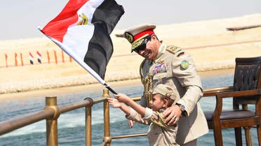 In this picture provided by the office of the Egyptian Presidency, Egyptian President Abdel-Fattah el-Sissi smiles at a boy dressed in a tiny military uniform as he waves the national flag from a monarchy-era yacht that sailed to the venue of a ceremony unveiling a major extension of the Suez Canal in Ismailia, Egypt, Thursday, Aug. 6, 2015. El-Sissi has billed the extension as an historic achievement needed to boost the country’s ailing economy after years of unrest. (Egyptian Presidency via AP)