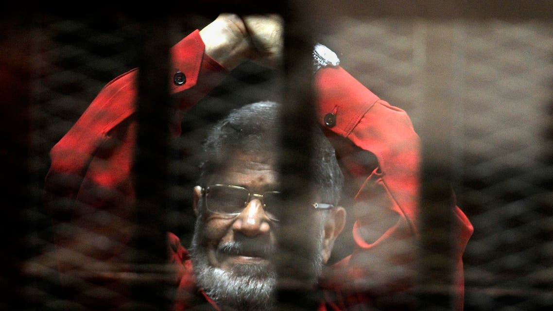 Ousted Egyptian President Mohammed Morsi, wearing a red jumpsuit that designates he has been sentenced to death, raises his hands inside a defendants cage in a makeshift courtroom at the national police academy, in an eastern suburb of Cairo, Egypt, Sunday, June 21, 2015