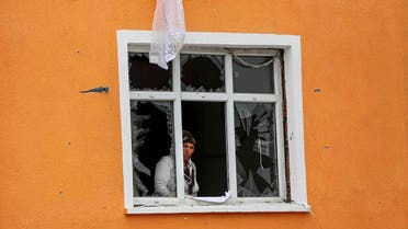 A woman looks on from her shattered window, damaged after an attack on a nearby police station in Istanbul