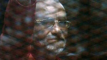 Muslim Brotherhood spiritual leader, Mohammed Badie wearing a red jumpsuit that designates he has been sentenced to death, waves from a defendants cage in a makeshift courtroom at the Torah prison, southern Cairo, Egypt, Tuesday, July 21, 2015. (AP Photo/Amr Nabil)