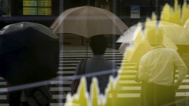 Pedestrians holding an umbrella are reflected on an electronic board showing the graph of the recent fluctuations of Japan's Nikkei average outside a brokerage in Tokyo, Japan, August 17, 2015. Japanese stocks rose on Monday morning on relief the contraction in the world's third-largest economy was not as bad as the market had expected. REUTERS/Yuya Shino