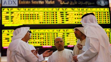 Investors speak in front of a screen displaying stock information at the Abu Dhabi Securities Exchange June 25, 2014. (Reuters)