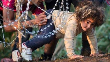 A refugee girl moves under barbed wire as she crosses from Serbia to Hungary, in Roszke, Thursday, Aug. 27, 2015. Over 10,000 migrants, including many women with babies and small children, have crossed into Serbia over the past few days and headed toward Hungary. (AP Photo/Darko Bandic)