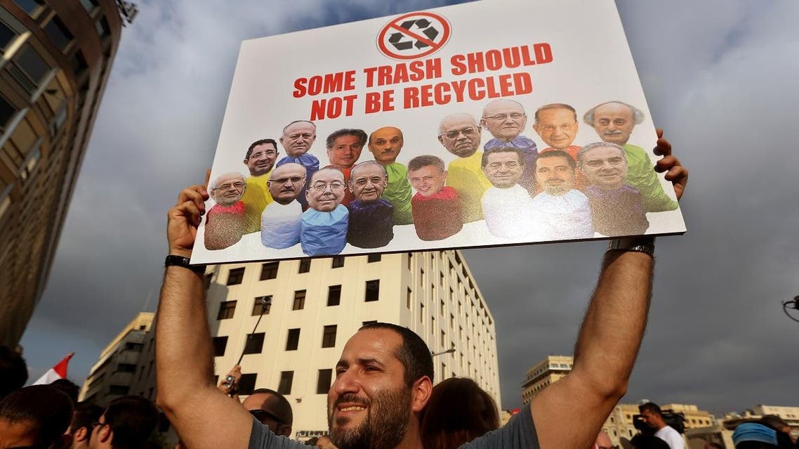 In this August 22, file photo, a Lebanese activist holds a poster with pictures of Lebanese Cabinet ministers during a protest against the ongoing trash crisis, in downtown Beirut. (AP)