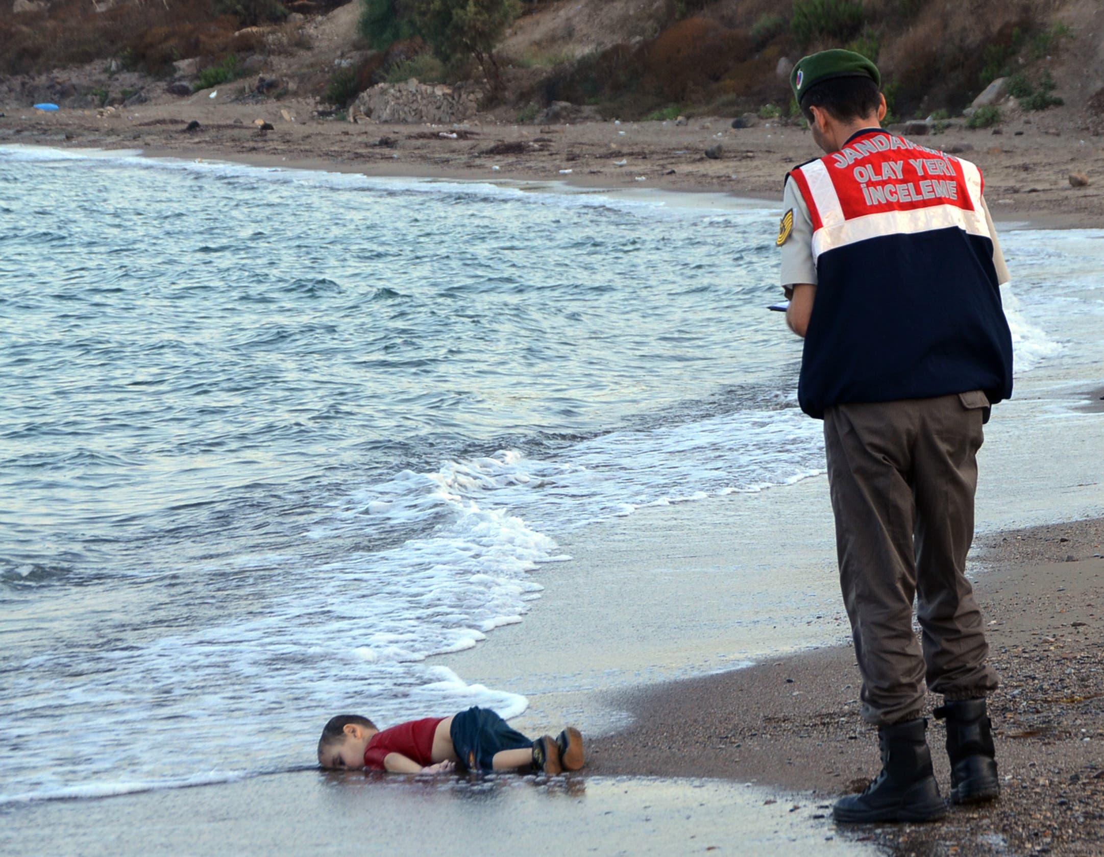A paramilitary police officer investigates the scene before carrying the lifeless body of Aylan Kurdi, 3, AP