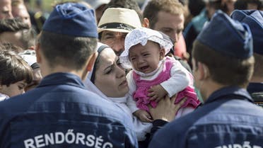 A migrant kisses a child who is crying as they stand in front of Hungarian police officers while waiting to board buses at a collection point in the village of Roszke, Hungary, September 7, 2015. Reuters
