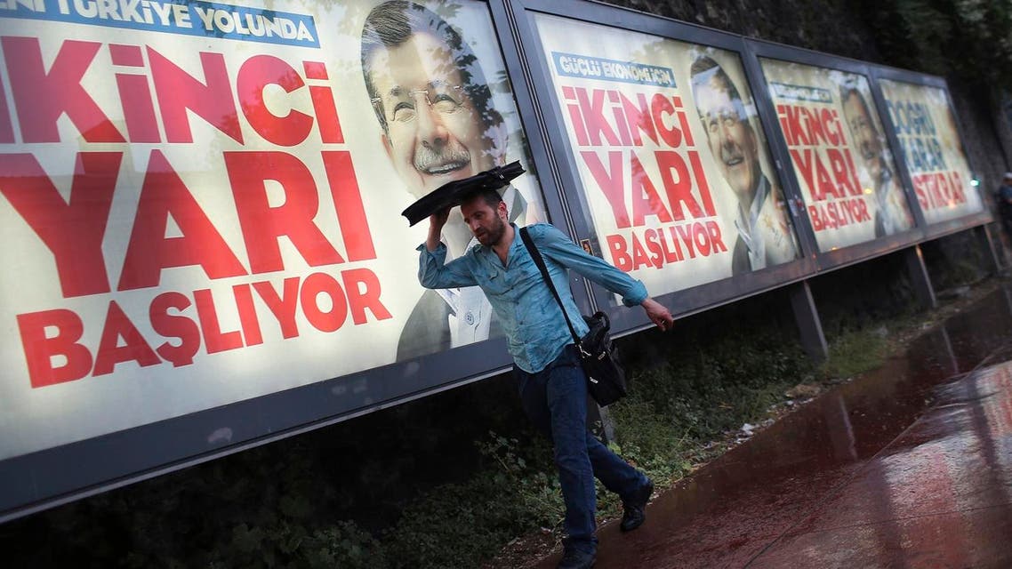 Under heavy rain, a man walks past billboards of Turkey's Prime Minister and leader of the Justice and Development Party (AKP) Ahmet Davutoglu in Istanbul, Turkey, Friday, June 5, 2015. (AP)