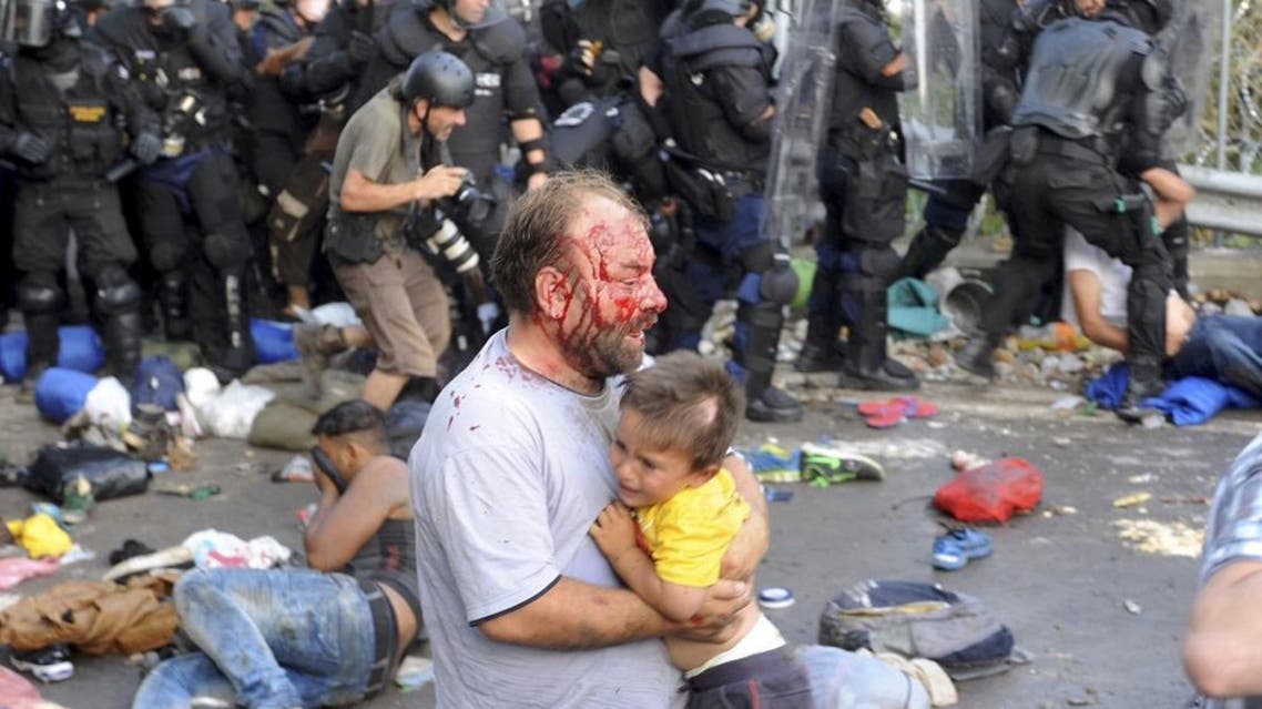 An injured migrant carries a child during clashes with Hungarian riot police at the border crossing with Serbia in Roszke, Hungary September 16, 2015. REUTERS