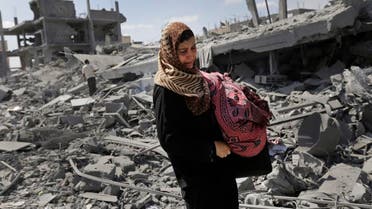 A Palestinian woman carries her belongings past the rubble of houses destroyed by Israeli strikes in Beit Hanoun, northern Gaza Strip, Saturday, July 26, 2014. AP