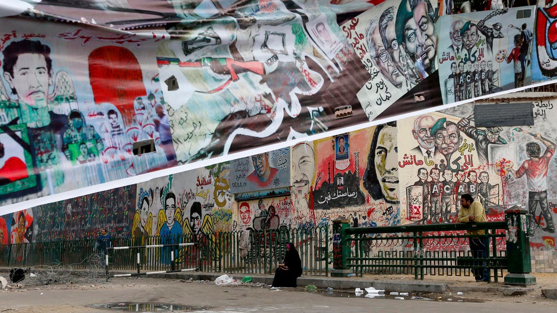 A woman sits near graffiti painted on a wall near Tahrir Square in Cairo, Egypt, Friday, Dec. 14, 2012. Opposing sides in Egypt's political crisis were staging rival rallies on Friday, the final day before voting starts on a contentious draft constitution that has plunged the country into turmoil and deeply divided the nation.(AP Photo/Petr David Josek)