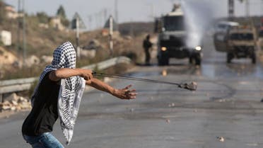 A Palestinian uses a sling shot to throw stones towards Israeli AP