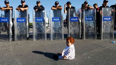 An infant sits on the road in front of a line of Turkish police who block migrants on a highway near Edirne, Turkey, September 19, 2015. Hundreds of mainly Syrian migrants remain blocked on western Turkey's border with Greece after camping for several days on the side of the highway. REUTERS/Osman Orsal