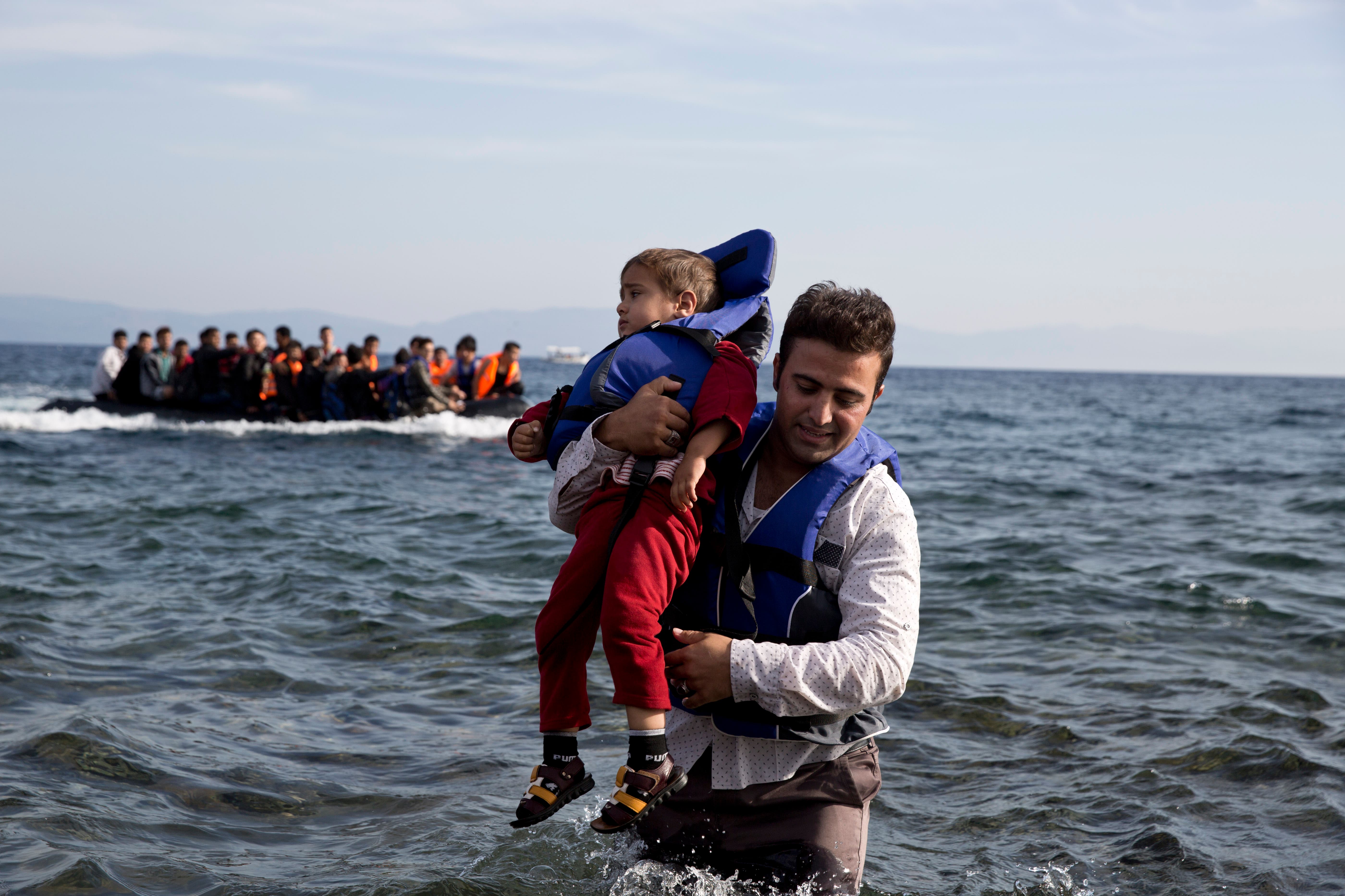 A Syrian refugee carries his child after they arrived from Turkey to the shores of the Greek island of Lesbos, on an inflatable dinghy, with another boat in the background, Saturday Sept. 26, 2015. More than 260,000 asylum-seekers have arrived in Greece so far this year, most reaching the country's eastern islands on flimsy rafts or boats from the nearby Turkish coast. (AP Photo/Petros Giannakouris)