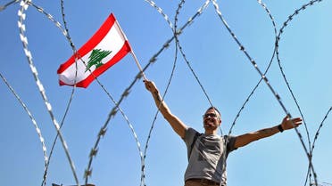A Lebanese anti-government protester is seen through barbed wire as he waves his national flag, on a road leading to the parliament building where Lebanese political leaders held their third dialogue session. (File photo: AP)