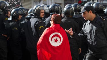 A Tunisian protester drapped in a national flag, argues with riot police officers during a rally. AP 