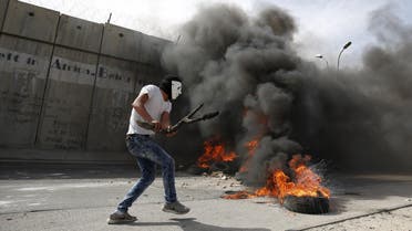 A masked Palestinian protester holds a wooden slingshot as he walks past a section of the Israeli barrier during clashes in the West Bank town of Al-Ram, near Jerusalem October 22, 2015. Nine Israelis have been killed in Palestinian stabbings, shootings and vehicle attacks since the start of October. Forty-nine Palestinians, including 25 assailants, among them children, have been killed in attacks and during anti-Israeli protests. Among the causes of the turmoil is Palestinians' anger at what they see as Jewish encroachment on the al-Aqsa mosque compound in Jerusalem's walled Old City. REUTERS/Mohamad Torokman TPX IMAGES OF THE DAY