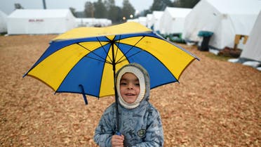 Three-year-old Yazem from Aleppo, Syria, holds an umbrella as he stands in front of tents in a refugee camp in Celle