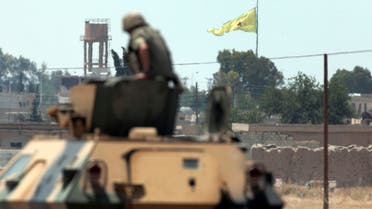 a Turkish soldier on an armoured personnel carrier watches as in the background a flag of the Kurdish People's Protection Units, or YPG, is raised over the city of Tal Abyad AP