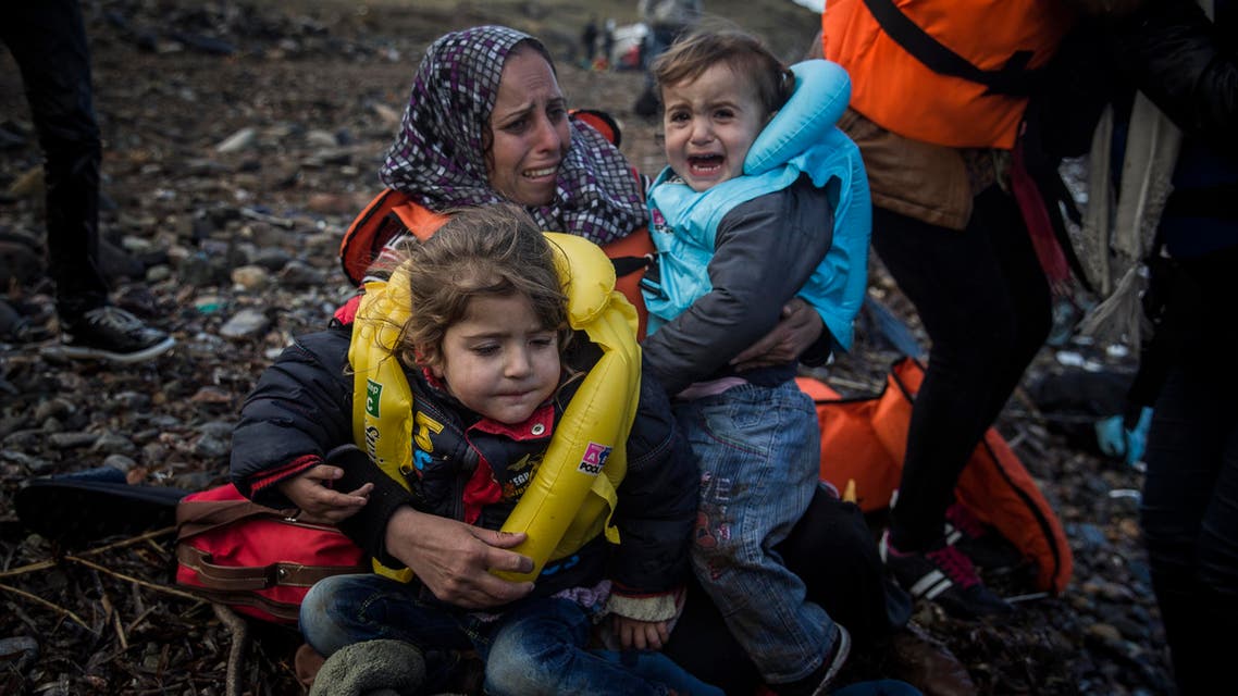 A woman holds two children on a beach after arriving on a dinghy from a Turkish coast to the northeastern Greek island of Lesbos, Sunday, Oct. 25, 2015.