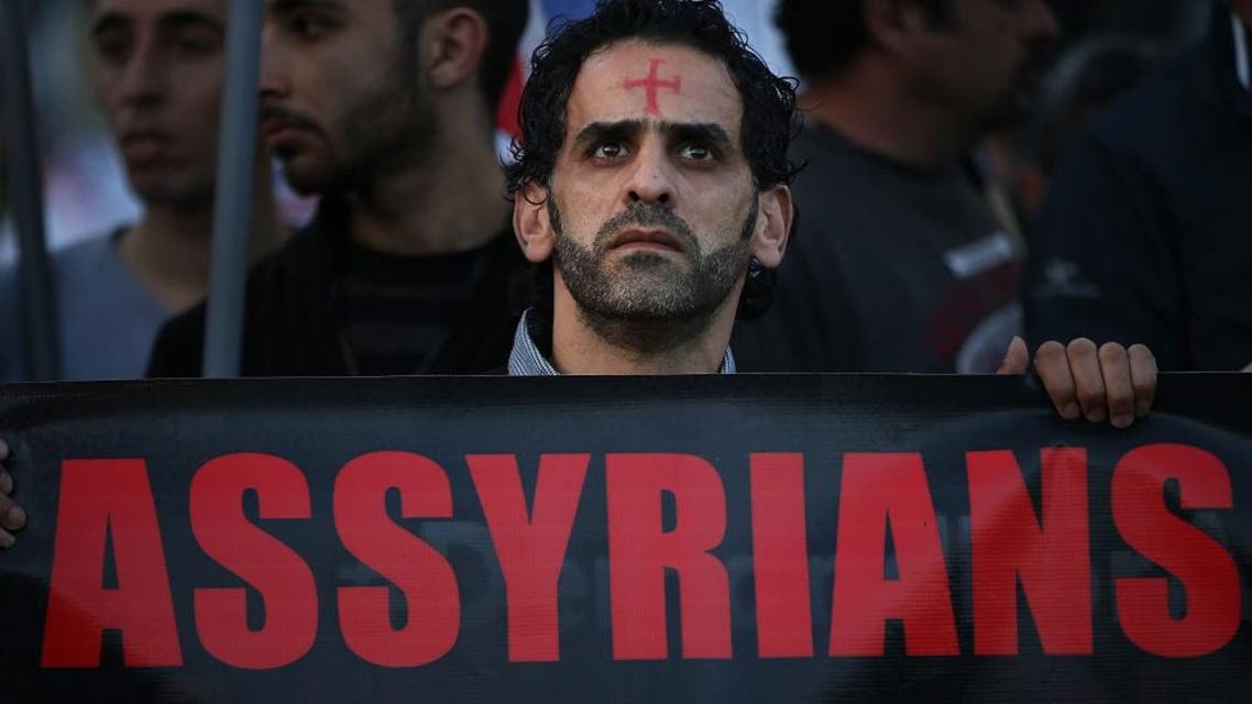 an Assyrian man with a red cross painted on his forehead holds a banner as he walks during a protest of several hundred people in solidarity with Christians abducted in Syria and Iraq. (File: AP)