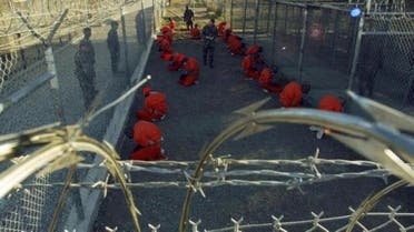 Detainees in orange jumpsuits sit in a holding area under the watchful eyes of military police during in-processing to the temporary detention facility at Camp X-Ray of Naval Base Guantanamo Bay in this January 11, 2002 file photograph. 