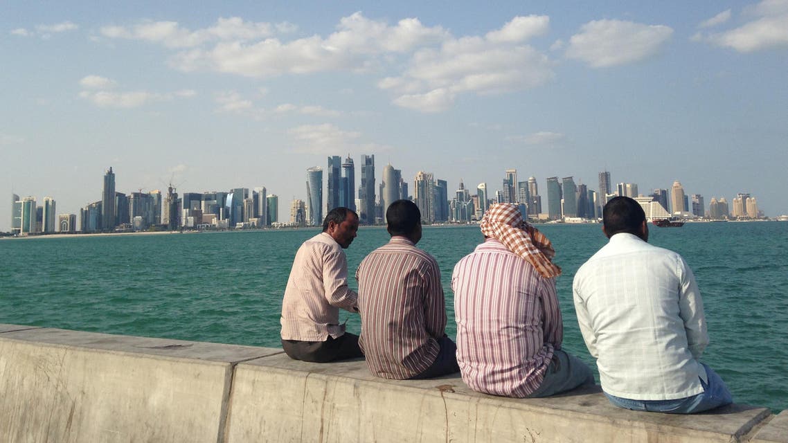 FILE - In this Nov. 7, 2014, file photo, men talk by the sea overlooking the Qatar skyline in Doha, Qatar. Amnesty International said Thursday, May 21, 2015, that Qatar is failing to deliver on reforms for its low-paid migrant workers a year after the wealthy Gulf nation announced plans to improve conditions for laborers building its highways, hotels, stadiums and skyscrapers. (AP Photo/Rob Harris, File)