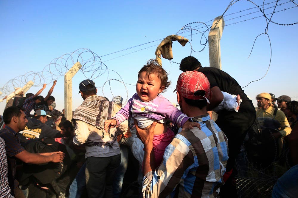 A Syrian refugee carries a baby after crossing over the broken border fence into Turkey from Syria in Akcakale, Sanliurfa province, southeastern Turkey, Sunday, June 14, 2015 | AP