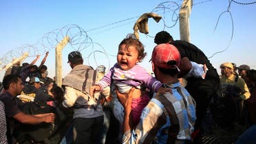 A Syrian refugee carries a baby after crossing over the broken border fence into Turkey from Syria in Akcakale, Sanliurfa province, southeastern Turkey, Sunday, June 14, 2015 | AP