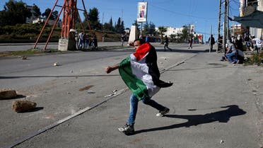 A Palestinian protester wearing a Palestinian flag uses a slingshot to hurl stones during clashes with Israeli soldiers in the West Bank village of Halhul, near Hebron. (File photo: AP)