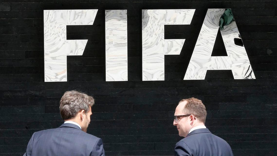Two men talk to each other in front of the FIFA logo at the FIFA headquarters in Zurich, Switzerland. (File photo: AP)