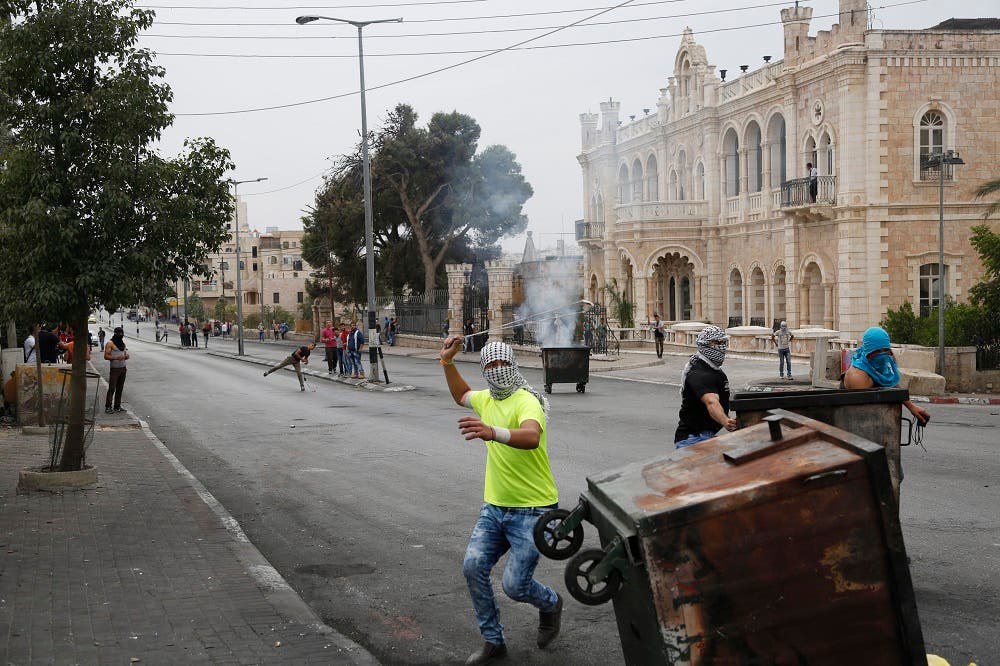 This Friday, Oct. 23, 2015 photograph shows Palestinians clashing with Israeli troops in front of the Intercontinental hotel in the West Bank city of Bethlehem. The century-old Jacir Palace hotel, with its soaring stone archways and wrought iron balconies, was once a symbol of Bethlehem’s wealth and tourism potential. Today, the property reflects the city’s dour mood ahead of the crucial Christmas season after months of unrest that has taken more than 100 lives, including a Palestinian waiter from the hotel. (AP Photo/Nasser Shiyoukhi)