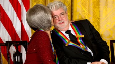 Actress and singer Rita Moreno, left, kisses filmmaker George Lucas on the cheek, as the 2015 Kennedy Center Honors honorees listen to President Barack Obama speak at the 2015 Kennedy Center Honors reception in the East Room of the White House in Washington, Sunday, Dec. 6, 2015. (AP)