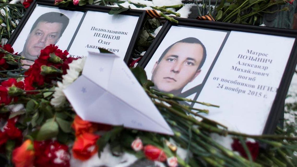 Photos of Lt.Col. Oleg Peshkov, left, and sailor Alexander Pozynich are placed at a monument to Soviet Officers with flowers and a toy jet made of paper outside Russian Army General Staff headquarters in Moscow, Russia, Thursday, Nov. 26, 2015. Peshkov was a pilot of Russian Su-24, which was shot down by Turkish air forces and Pozynick took part in a rescue operation, both were killed. (AP Photo/Ivan Sekretarev)