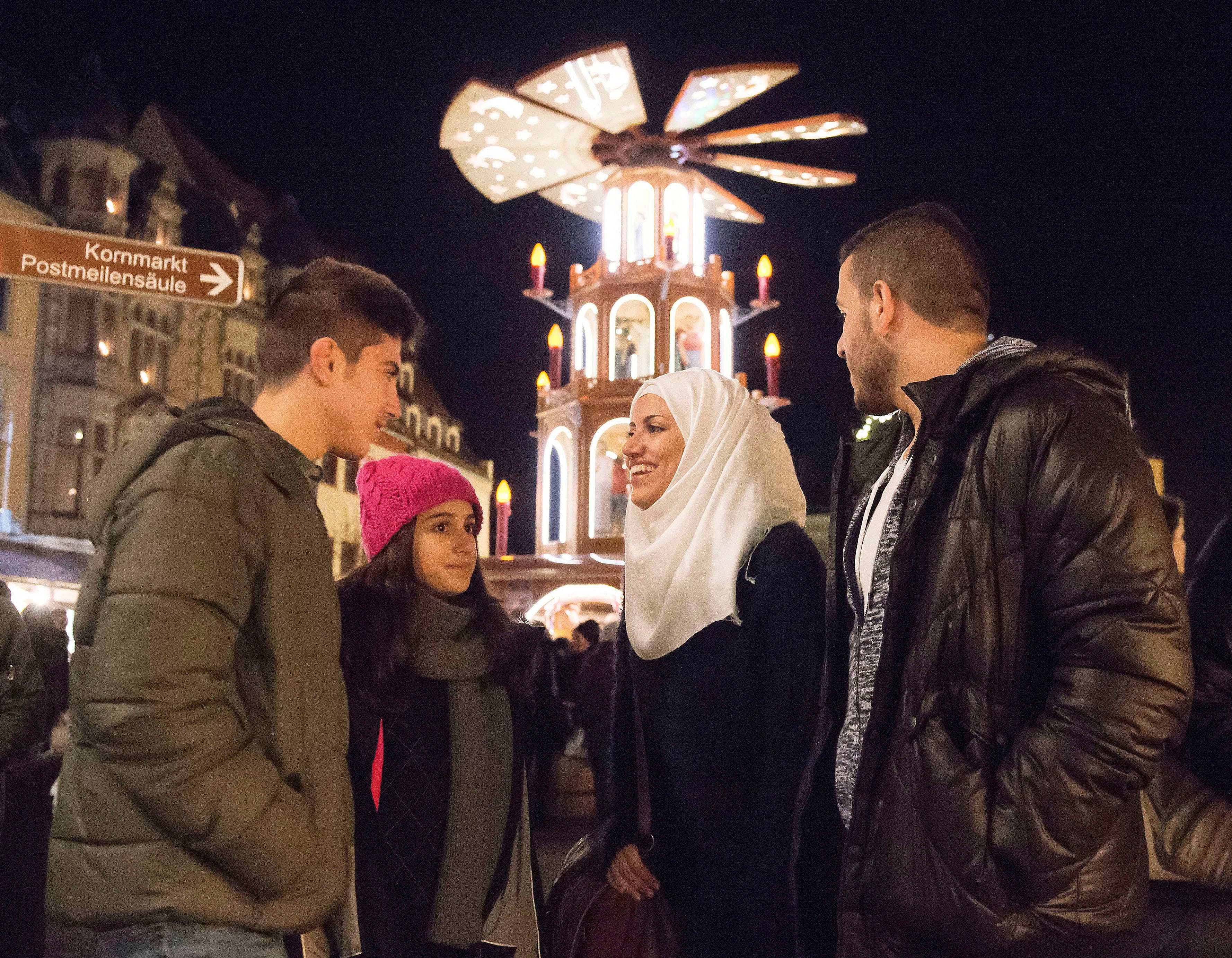 In this photo taken Tuesday, Dec. 8, 2015, Syrian refugees Yaman Habashieh, Raghad Habashieh, Reem Habashieh and Mohammed Habashieh, from left to right, visit the Christmas market in front of a wooden traditional pyramid in Zwickau, eastern Germany.