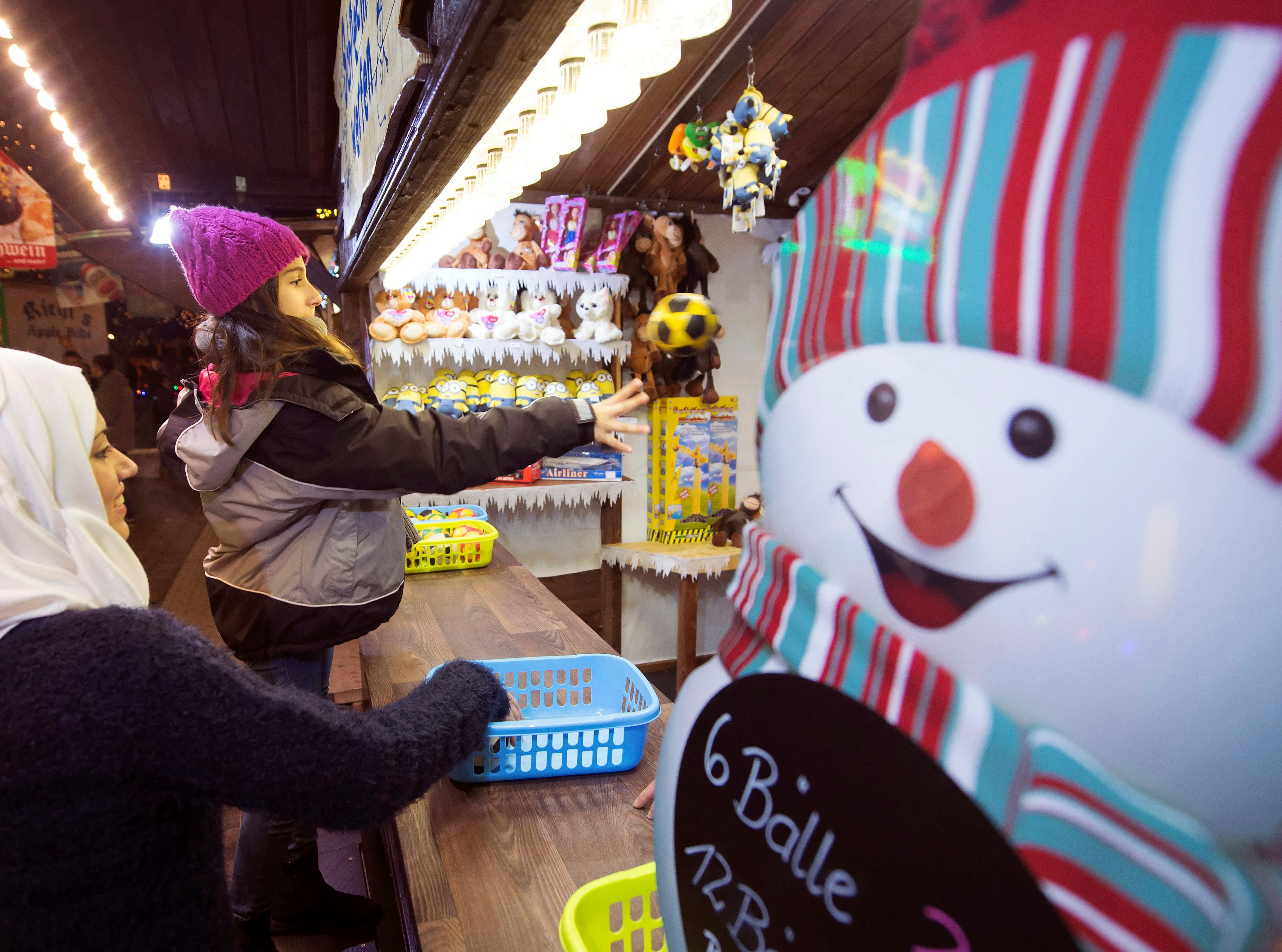 In this photo taken Tuesday, Dec. 8, 2015, Syrian refugee Raghad Habashieh, right, plays a ball besides her sister Reem Habashieh, left, as they visit the Christmas market in Zwickau, eastern Germany.