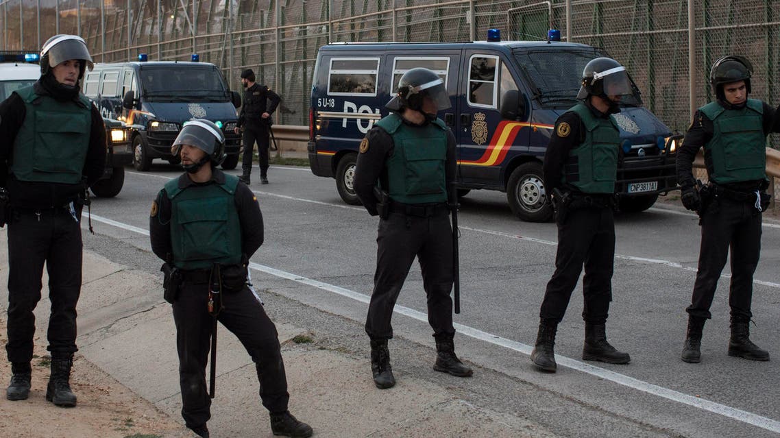 Police officers cordon off the area as sub-Saharan migrants climb over a metallic fence that divides Morocco and Melilla, another Spanish enclave. (AP)