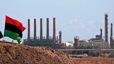 A Libyan rebel sits next to the country's flag as he guards outside the refinery in Ras Lanuf, eastern Libya. (Reuters)