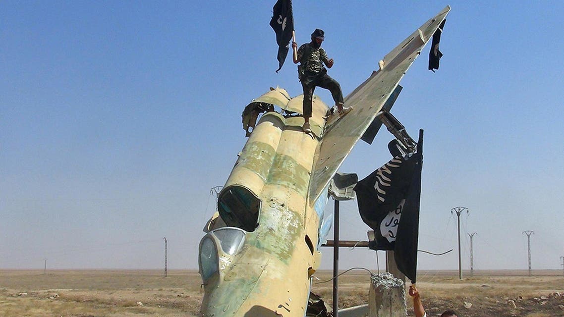 In this undated file photo posted on Wed. Aug. 27, 2014 by the Raqqa Media Center of ISIS, which has been verified and is consistent with other AP reporting, fighters of the Islamic State wave the group's flag from a damaged display of a government fighter jet, in Raqqa, Syria. AP
