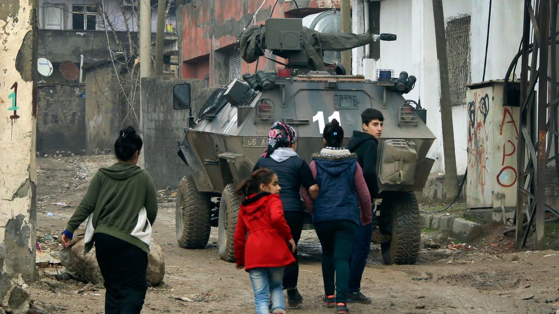 Backdropped by a Turkish forces armoured personnel carrier, residents walk around after the 24-hour curfew was lifted, in the mostly-Kurdish town of Silopi, in southeastern Turkey, near the border with Iraq, Tuesday, Jan. 19, 2016. AP