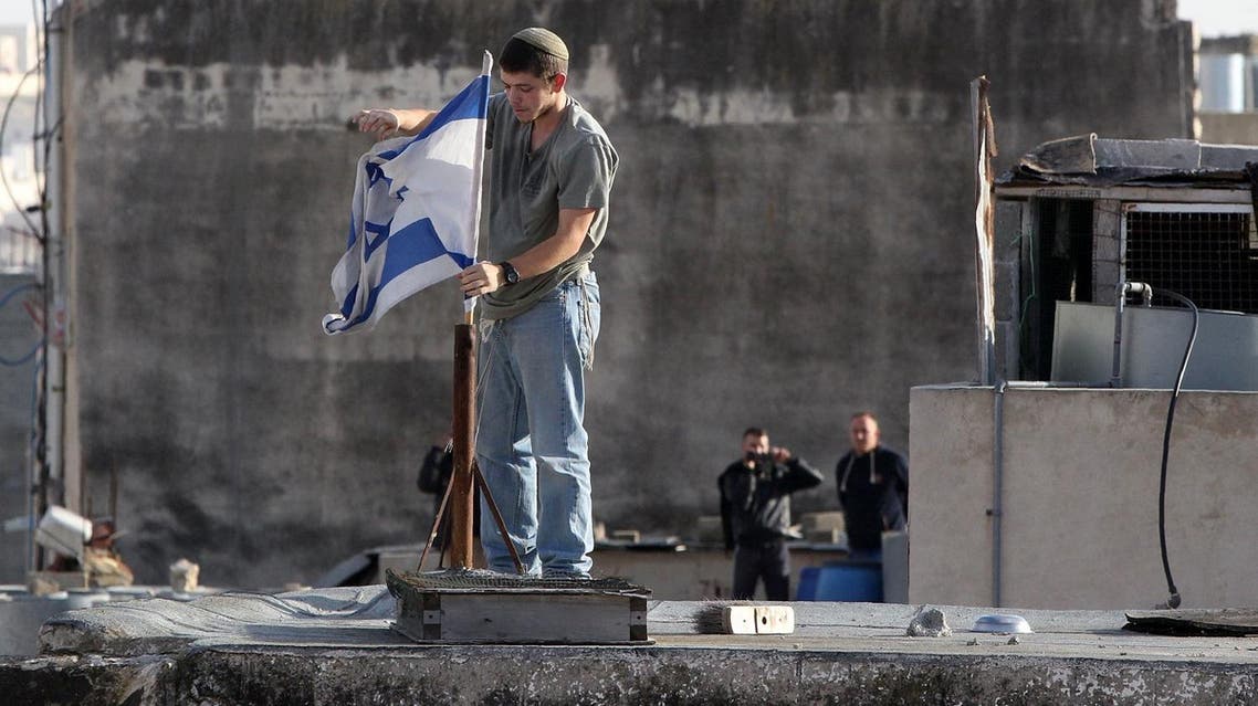 An Israeli settler fixes an Israeli flag on the roof of a building after dozens of settlers entered two homes in a building in the centre of the Palestinian city Hebron. (AFP)