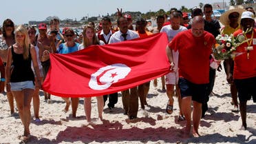 Tourists and residents, some displaying a Tunisian flag, walk on the beach to the scene of the attack in Sousse, Tunisia. (AP)