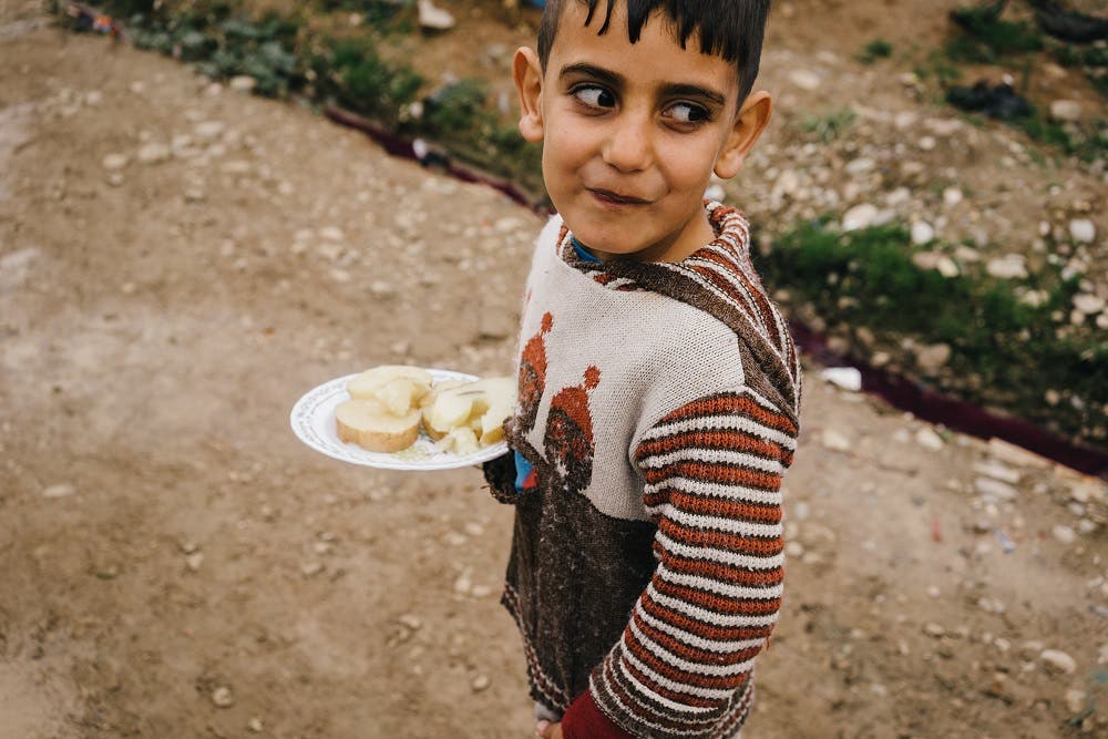 In this Sunday, Jan. 24, 2016 photo, a Syrian boy walks in Kawergosk refugee camp in northern Iraq carrying a plate with boiled potatoes. According to the U.N. children’s agency, malnutrition is a major threat among millions of refugees, as people eat less to conserve the little food they do have. (AP Photo/Alice Martins)