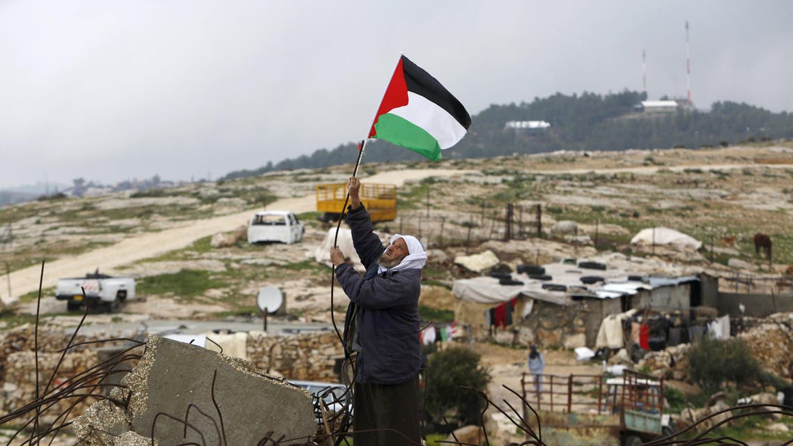 A Palestinian man hangs a Palestinian flag atop the ruins of a mosque, during a snow storm in West Bank village of Mufagara, south of Hebron January 27, 2016. REUTERS