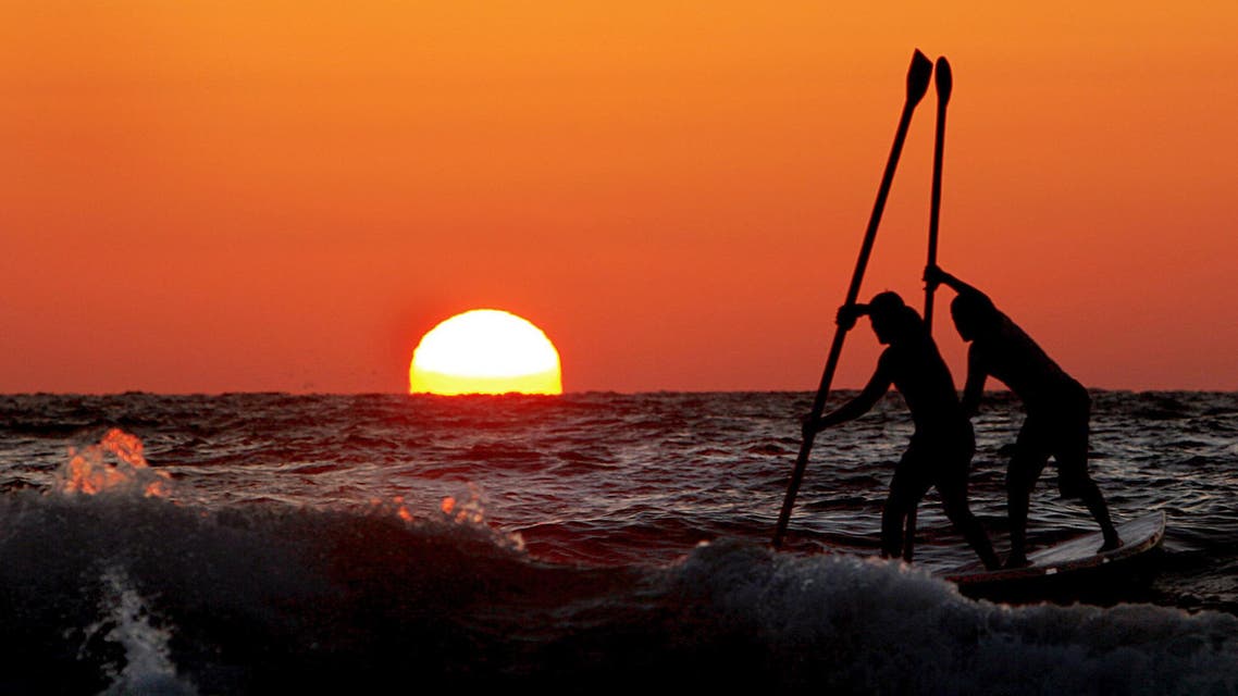 The sun sets as two young Palestinians paddle on a board on the Mediterranean on the Gaza City beach front, Saturday June 17, 2006.
