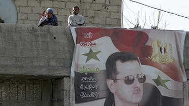 Residents stand near a picture of Syria's president Bashar al-Assad in Wafideen Camp, which is controlled by Syrian government forces, in Damascus suburbs, Syria February 13, 2016 (Reuter)
