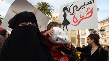   A Moroccan holding her child walks past supporters of the February 20 pro-reform movement to mark the fifth anniversary of the movement's creation, on February 20, 2016 in the capital Rabat (AFP)