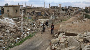 A boy rides a bicycle past a man sitting on rubble of a damaged house in the rebel held historic southern town of Bosra al-Sham, Deraa. (Reuters)